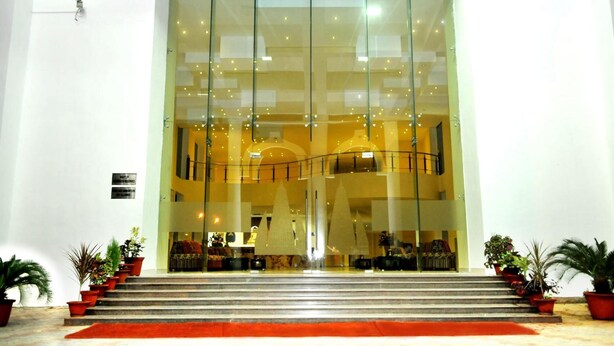 L’entrée d’un hôtel, avec une façade en verre, des marches menant à l’entrée et des plantes en pot de chaque côté.