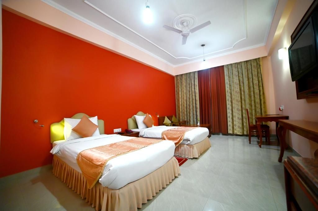 Une chambre d’hôtel avec deux lits, un ventilateur de plafond, une télévision et un coin repas.