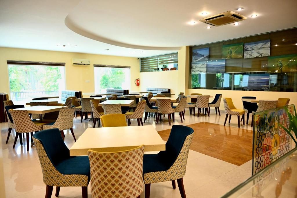 Un comedor amplio con varias mesas y sillas, ventanas grandes y un diseño moderno en el techo.