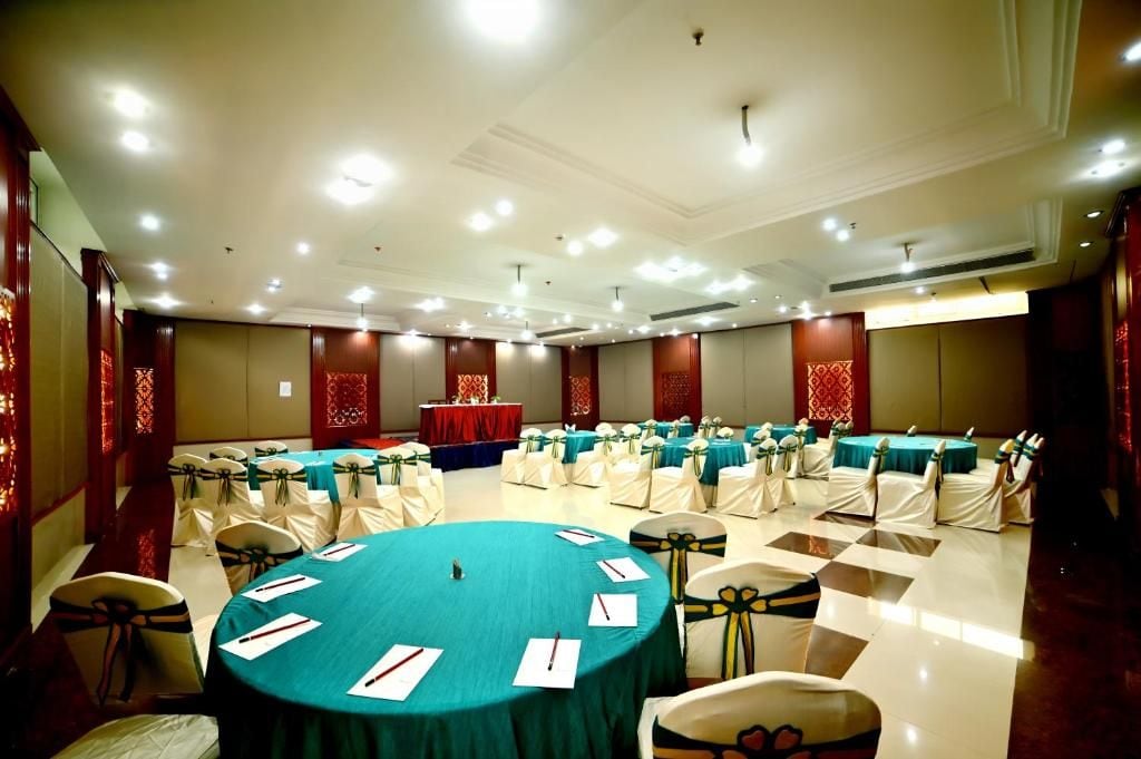A conference room with round tables, chairs, and a stage with a red backdrop.