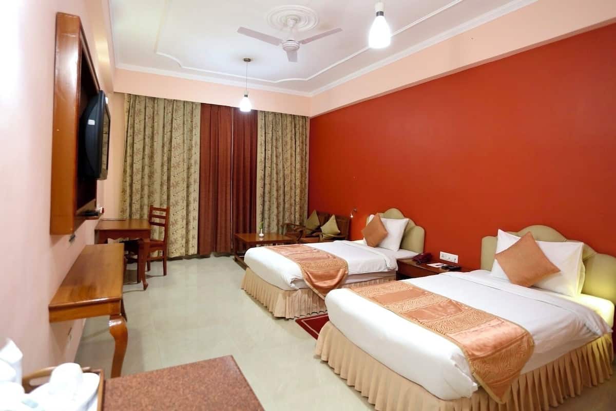 Quarto de hotel com duas camas, uma escrivaninha, uma cadeira, uma televisão e um ventilador de teto.