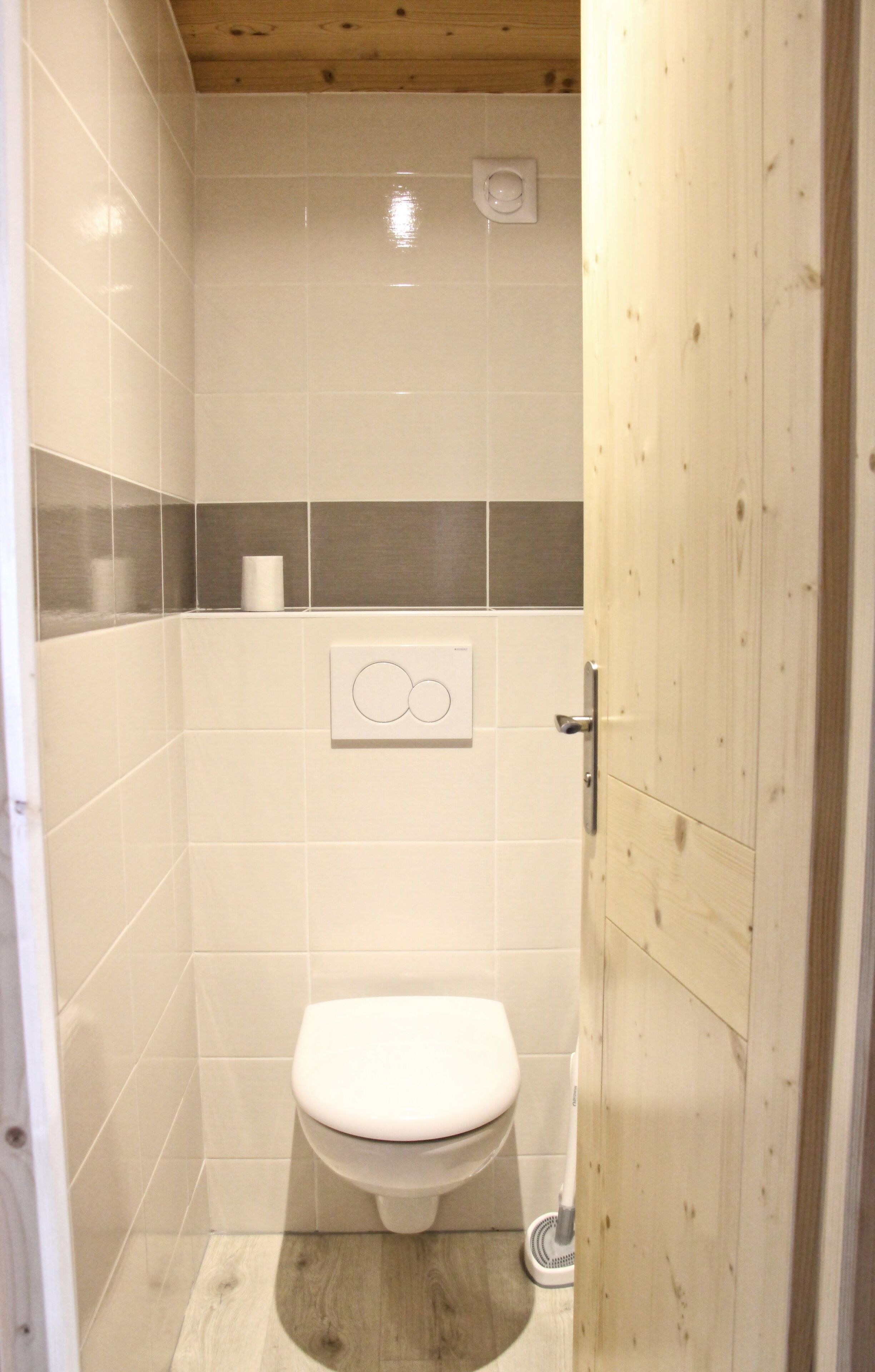 Un baño pequeño y cerrado con inodoro, secamanos y un accionador de descarga en la pared.