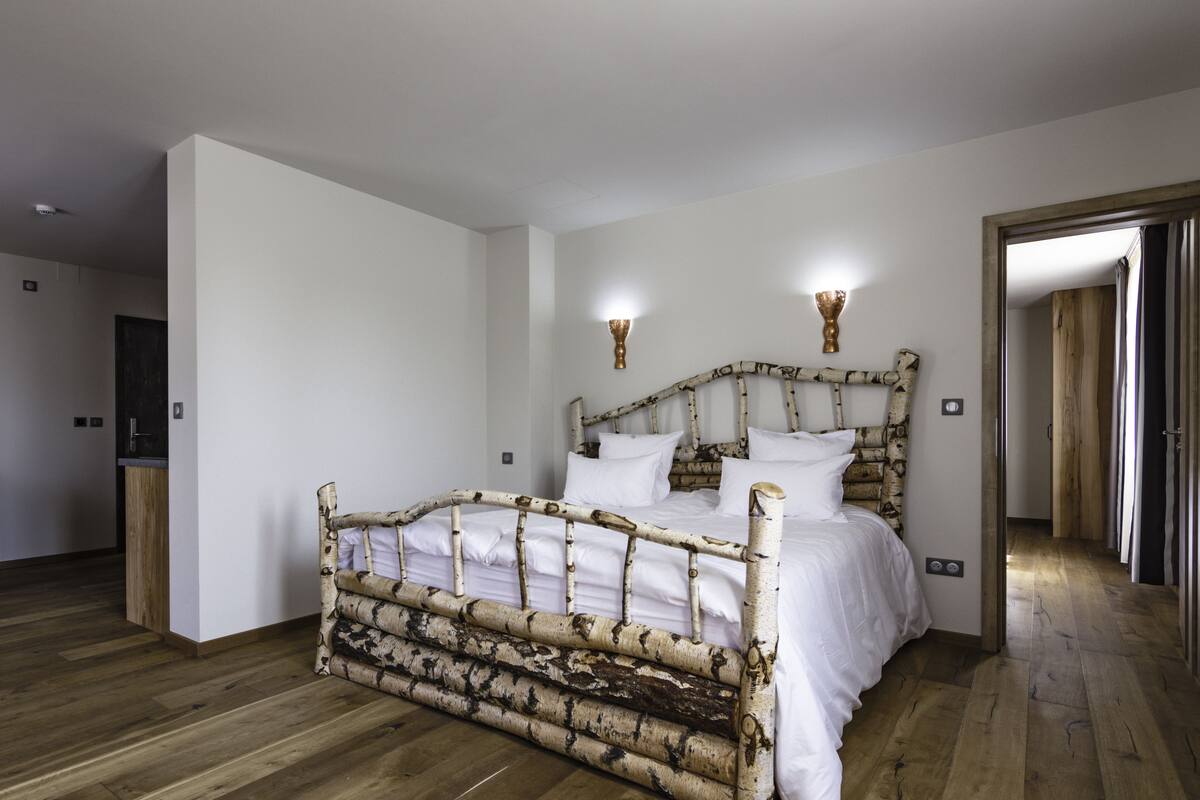 A bedroom with a rustic birch-patterned bed, white bedding, and a wooden floor.