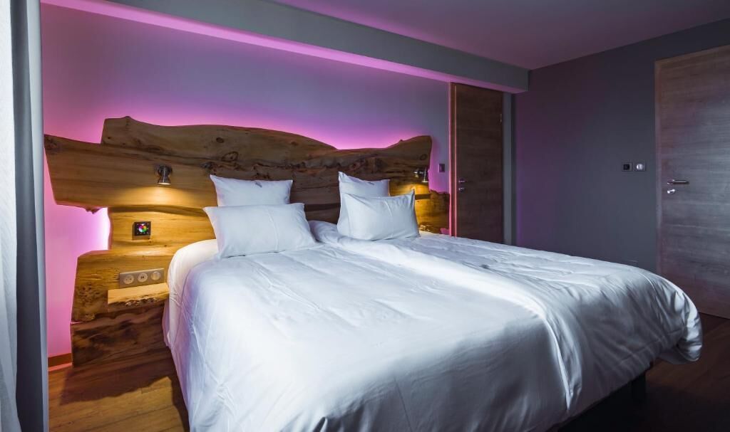 Een slaapkamer met een houten hoofdeinde, een bed met witte beddengoed en een nachtkastje met een lamp.