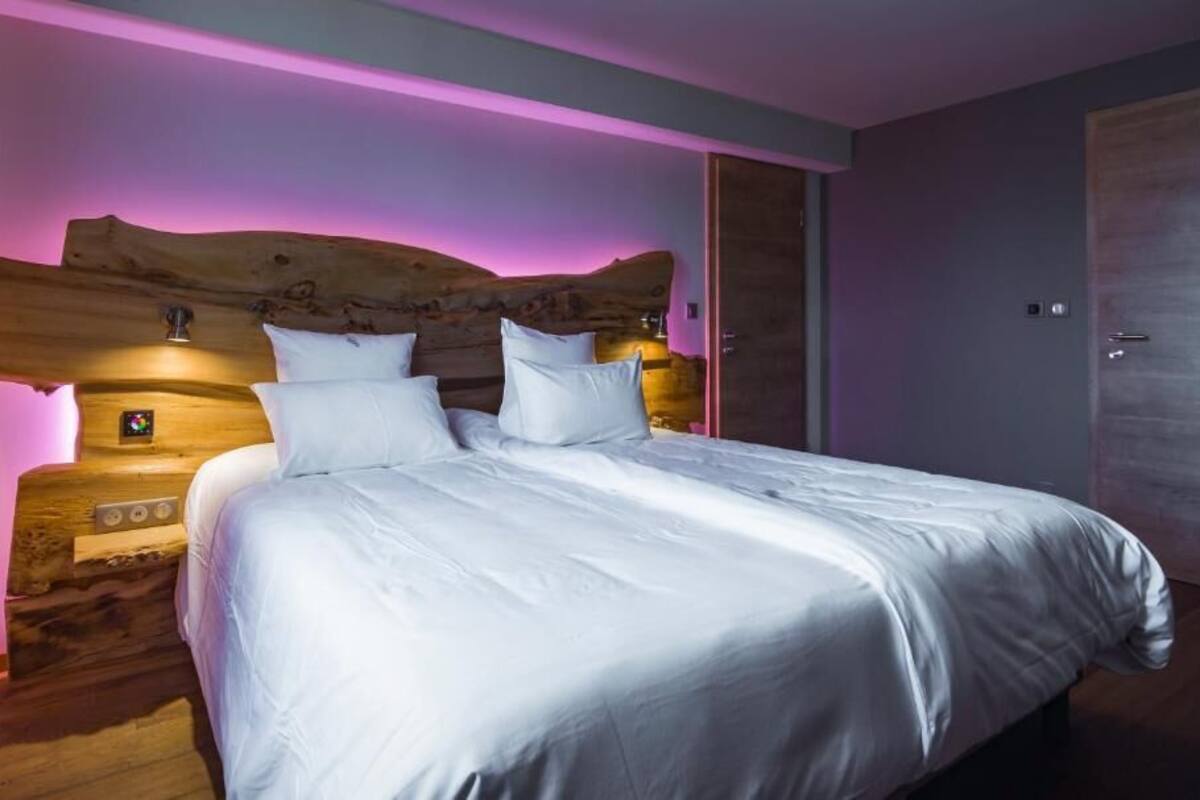 A bedroom with a wooden headboard, a bed with white bedding, and a nightstand with a lamp.