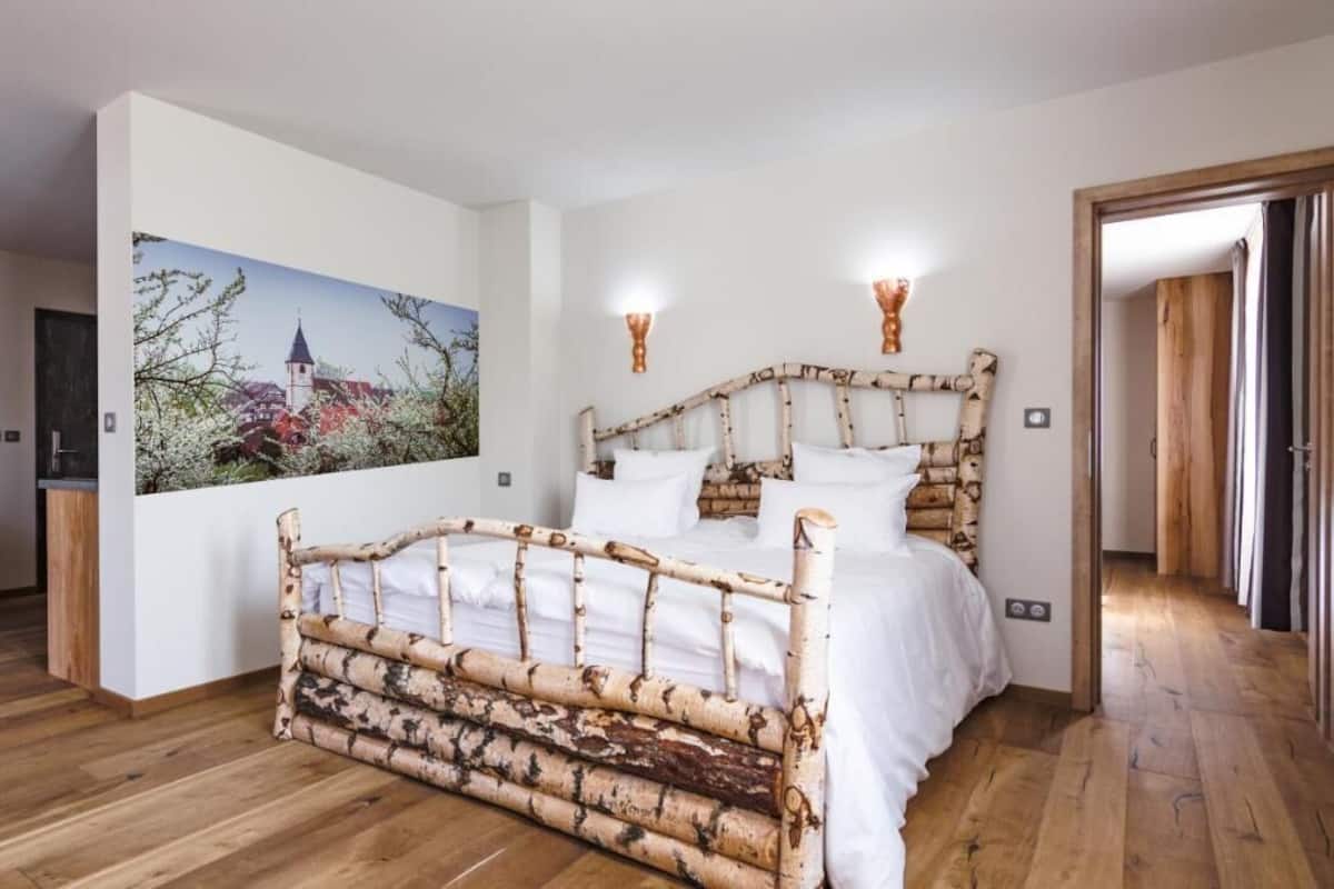 A bedroom with a wooden bed frame, a painting on the wall, and a wooden floor.