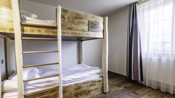 Ein Stockbett mit einem Holzkopfteil und einer Plakette, ein Fenster mit leichtem Vorhang und ein Holzboden.