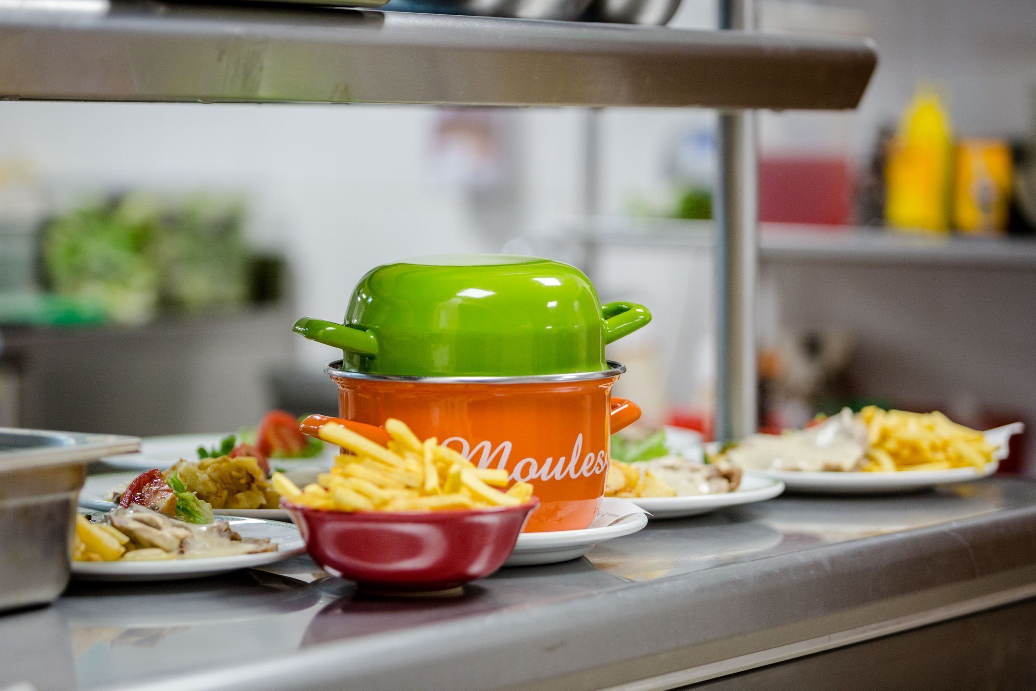 Una encimera de cocina con varios platos, incluyendo una olla verde y un bol rojo con papas fritas.
