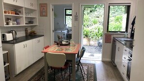 A compact kitchen with white cabinets, a dining table with chairs, a rug, and a view of greenery outside.