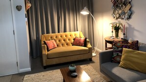 A living room with a yellow sofa, a grey sofa, a coffee table, a floor lamp, and a wall-mounted photo collage.