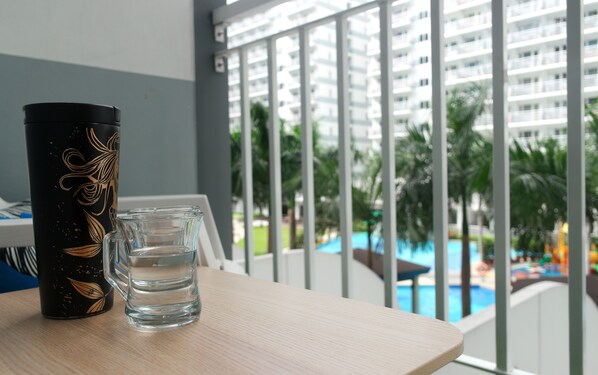 A table with a decorative tumbler and a glass of water, overlooking a pool and a high-rise building.