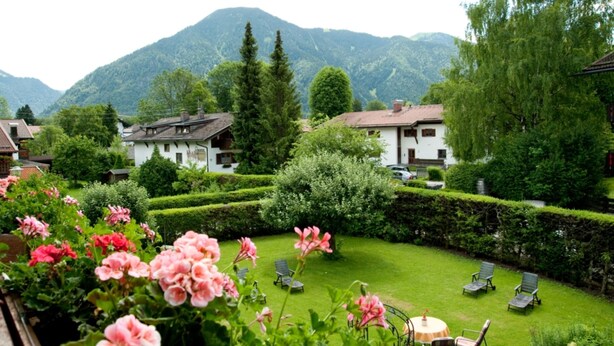 Un jardin avec des haies soigneusement taillées, une pelouse et un espace aménagé pour s’asseoir à l’extérieur.