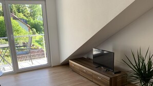 A modern living room with a wooden floor, a built-in entertainment unit with a flat-screen TV, and a sliding glass door leading to an outdoor patio. - Silvia’s Apartment 2 with a lake view (Goldbach)