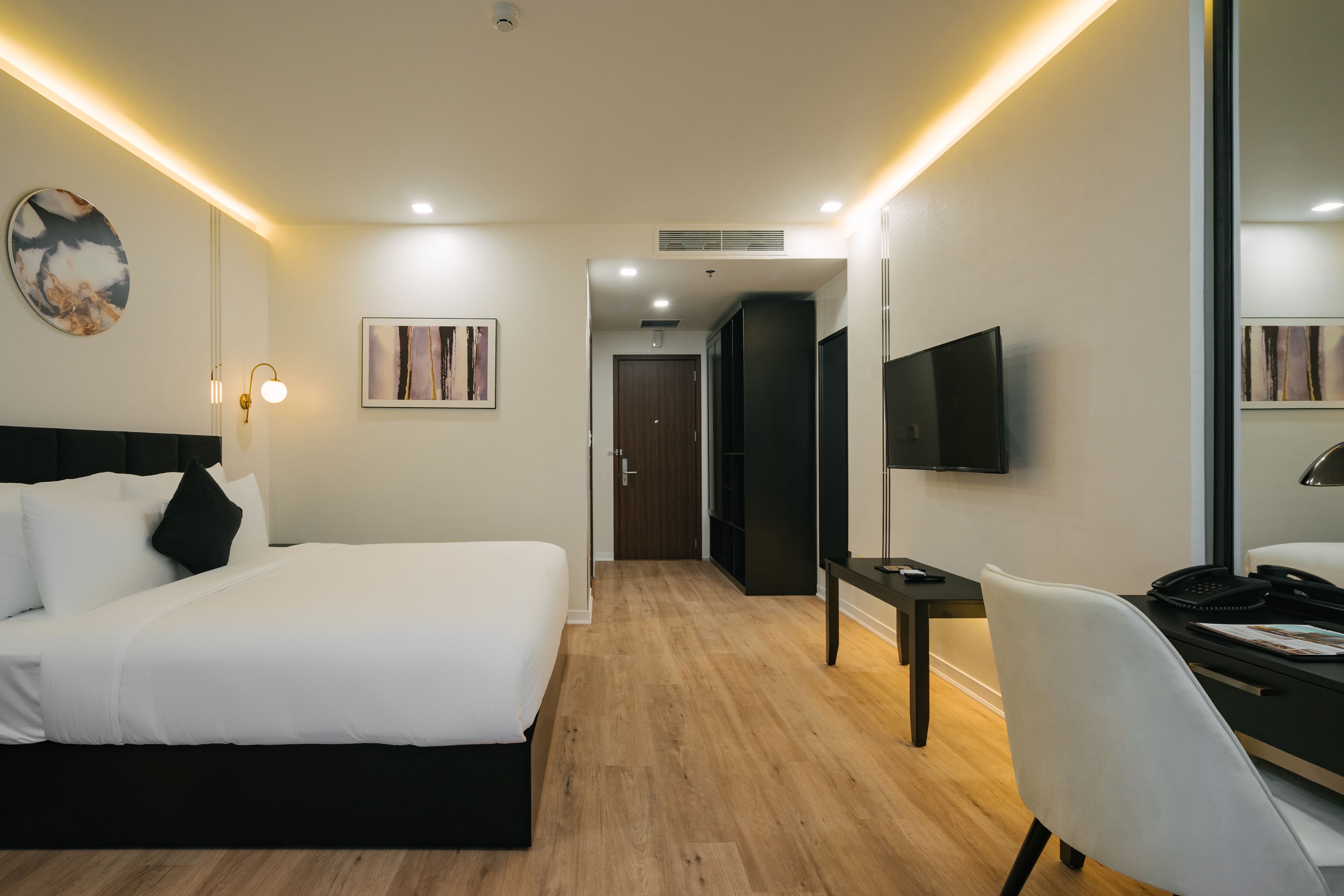 A hotel room with a bed, desk, chair, TV, and artwork on the walls.