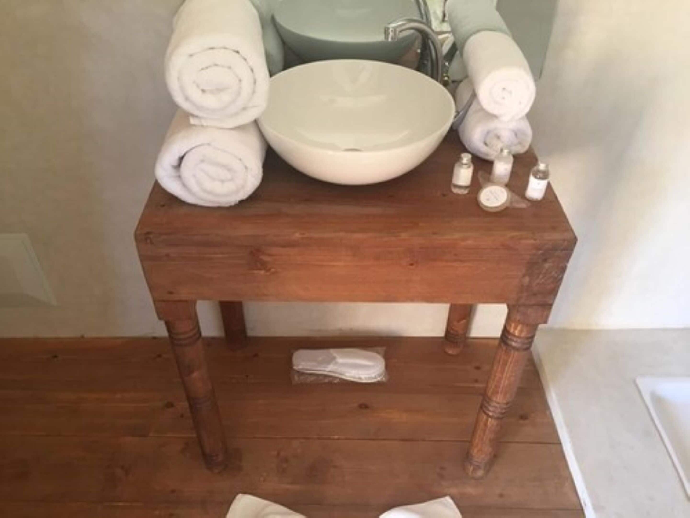 A wooden vanity with a white sink, rolled towels, and toiletries.