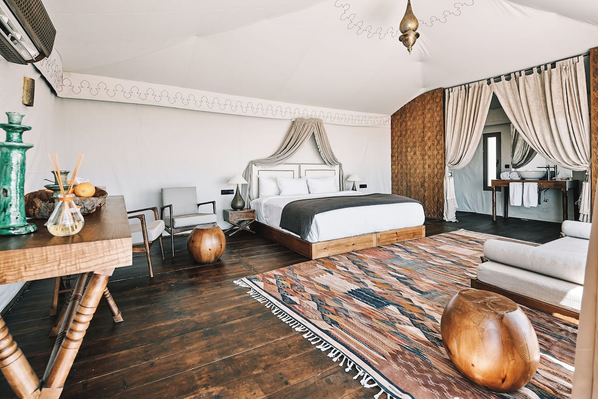 A modern hotel room with a large bed, a wooden side table, a dining table, and a sofa.