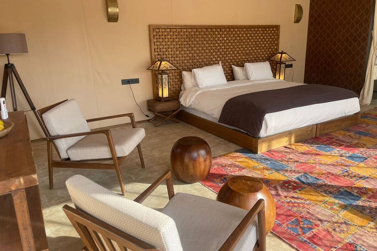 A hotel room with a large bed, two bedside tables with lamps, a desk with a chair, and a colorful rug.