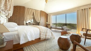 A spacious bedroom with a large bed, a view of the hills, and a balcony with seating. - The White Camel Lodge (Agafay)