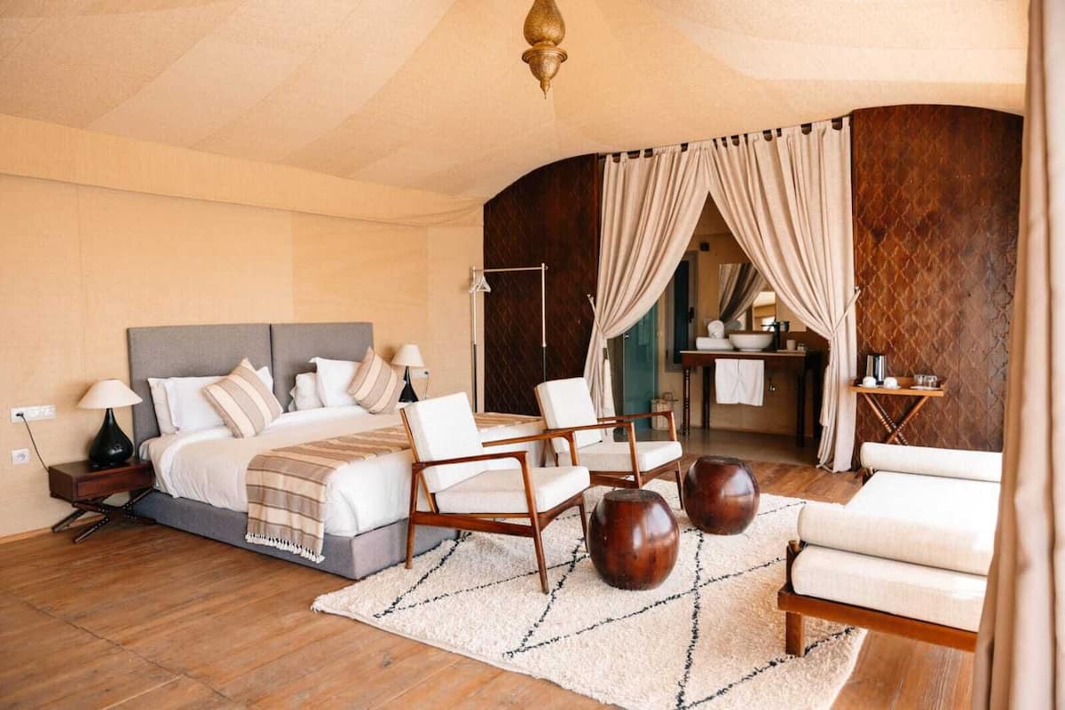 A spacious bedroom with a large bed, two chairs, a small table, and a view of a bathroom.