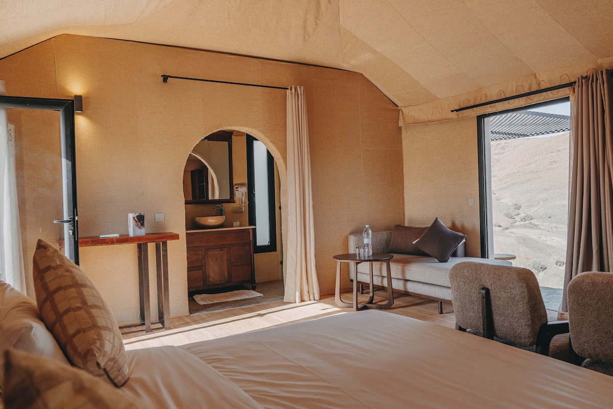 A room with a bed, a desk, a chair, and a large window with curtains.