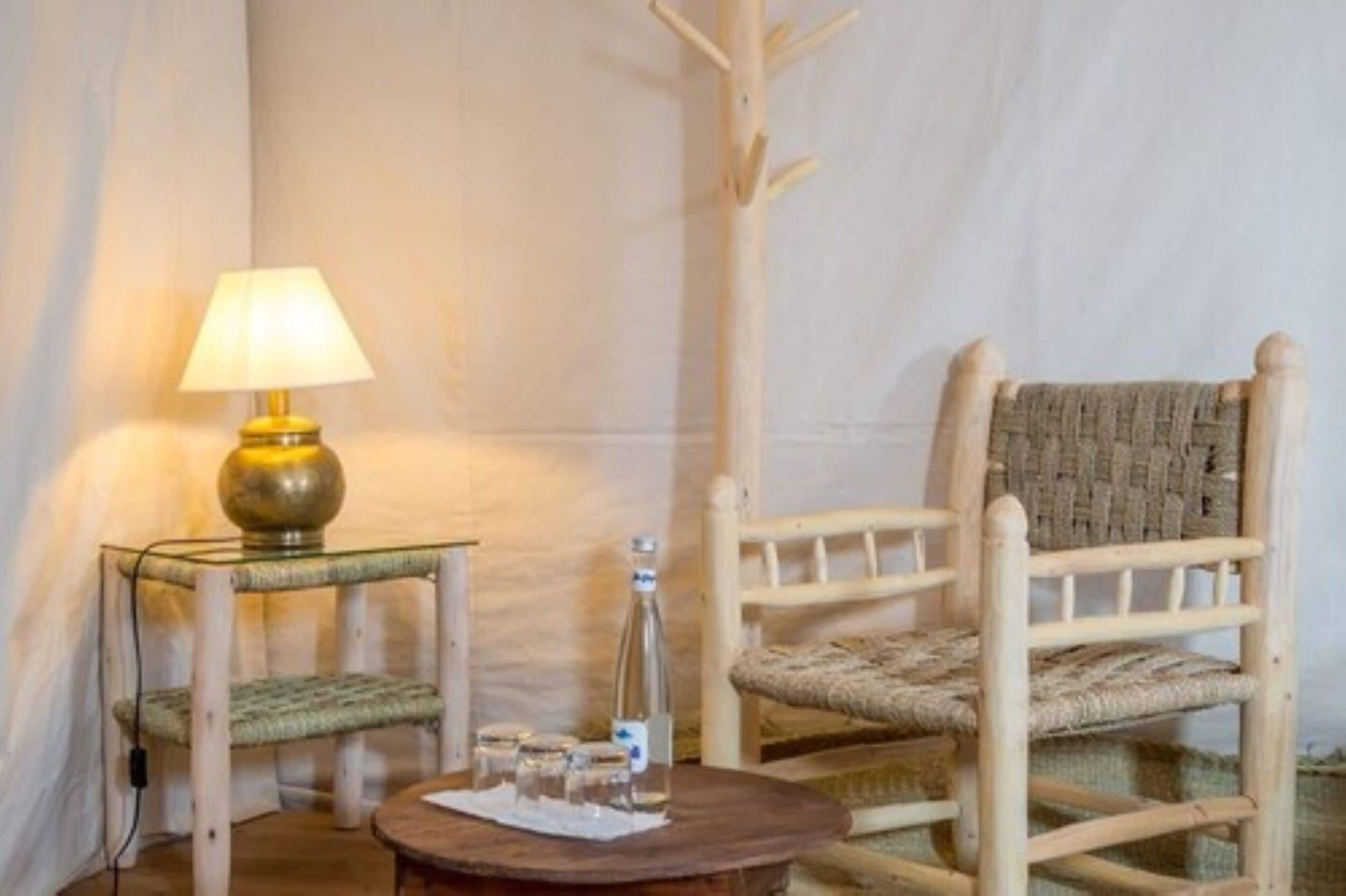 A cozy room with a wooden chair, a small table with a lamp, and a bottle of water.
