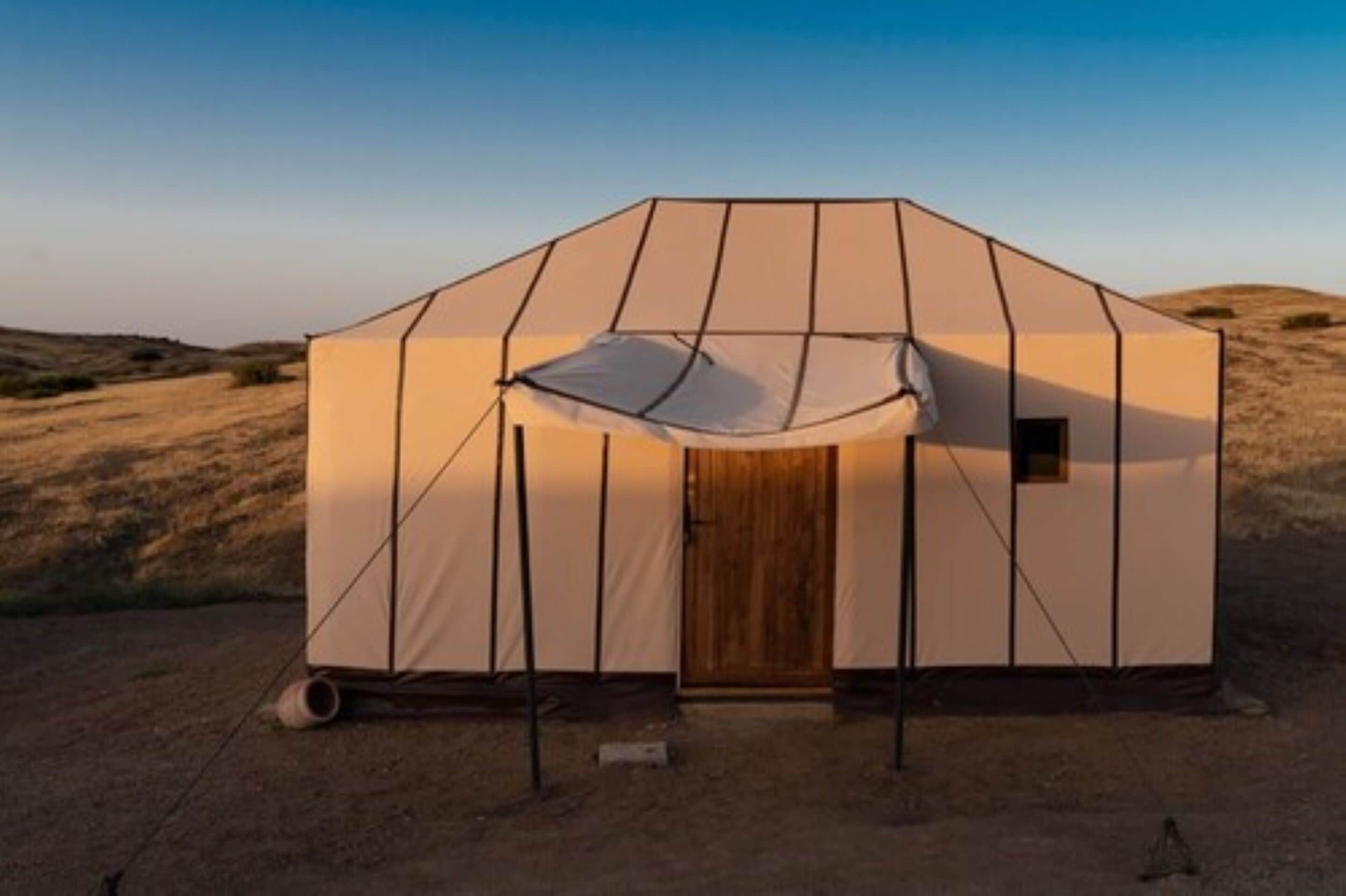 A tent-like structure with a door and a small window, set in a desert landscape.