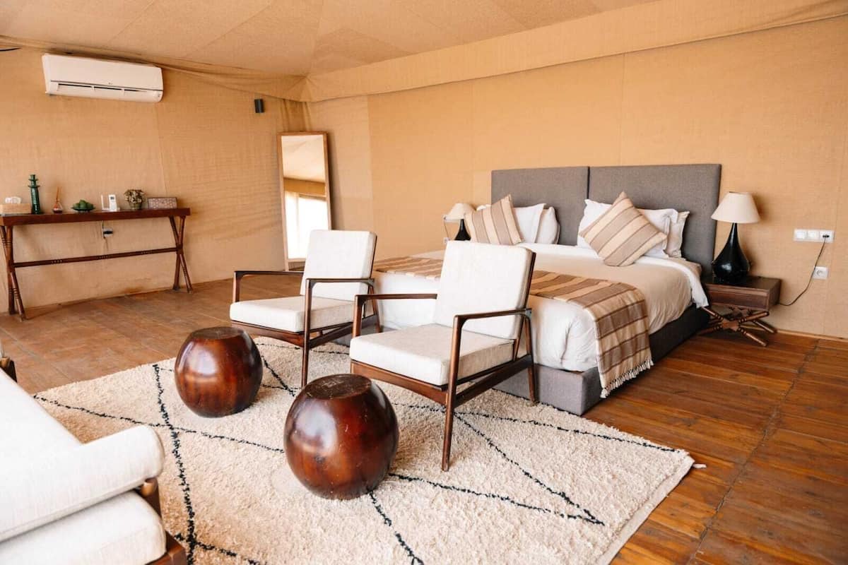 A bedroom with a bed, two chairs, a bedside table, a lamp, and a decorative rug.
