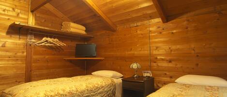 A cozy cabin-style room with two beds, a TV on a shelf, and a lamp on a nightstand.