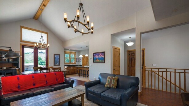 Ein geräumiger Wohnbereich mit Holzboden, einer großen Kronleuchter, einem roten Sofa, einem blauen Sofa und einem Couchtisch aus Holz.