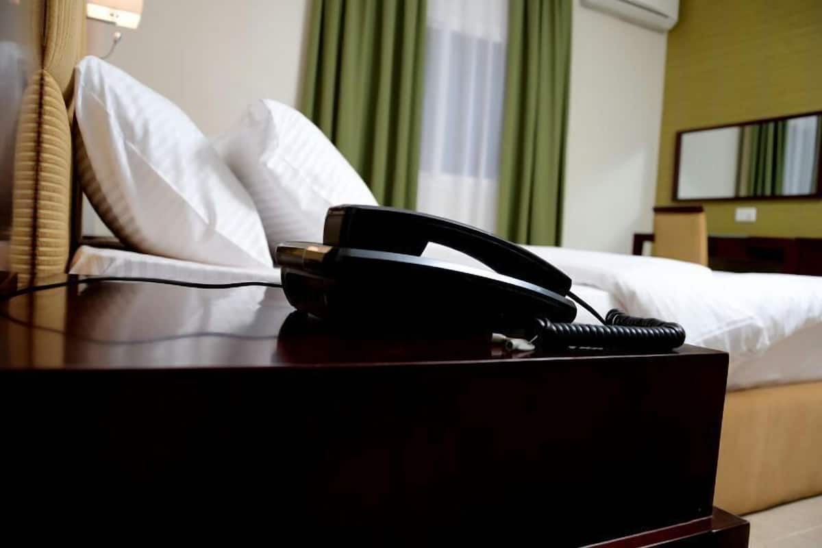 Habitación de hotel con cama, mesita de noche con teléfono y un espejo en la pared.