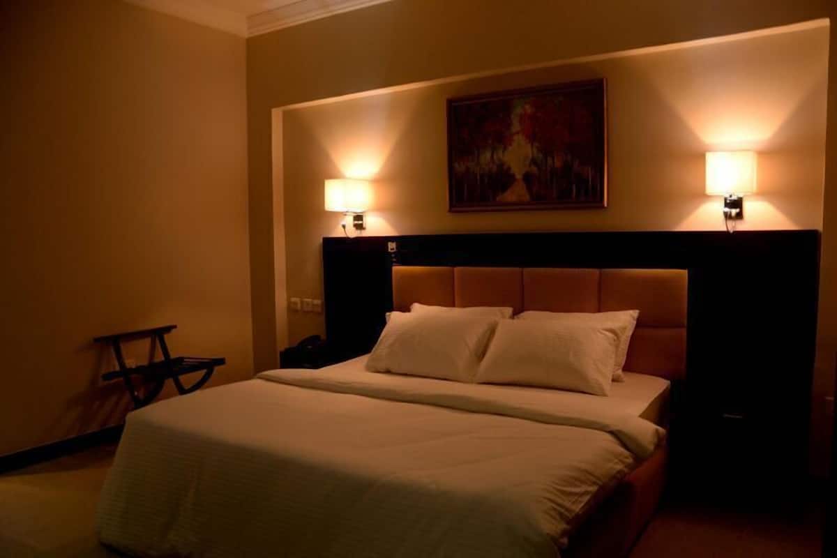 Una habitación de hotel con una cama grande, dos lámparas de noche, un cuadro en la pared y una mesita.