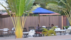 Un espace extérieur aménagé avec des tables et des chaises, entouré d’une clôture en bois et de plantes tropicales.