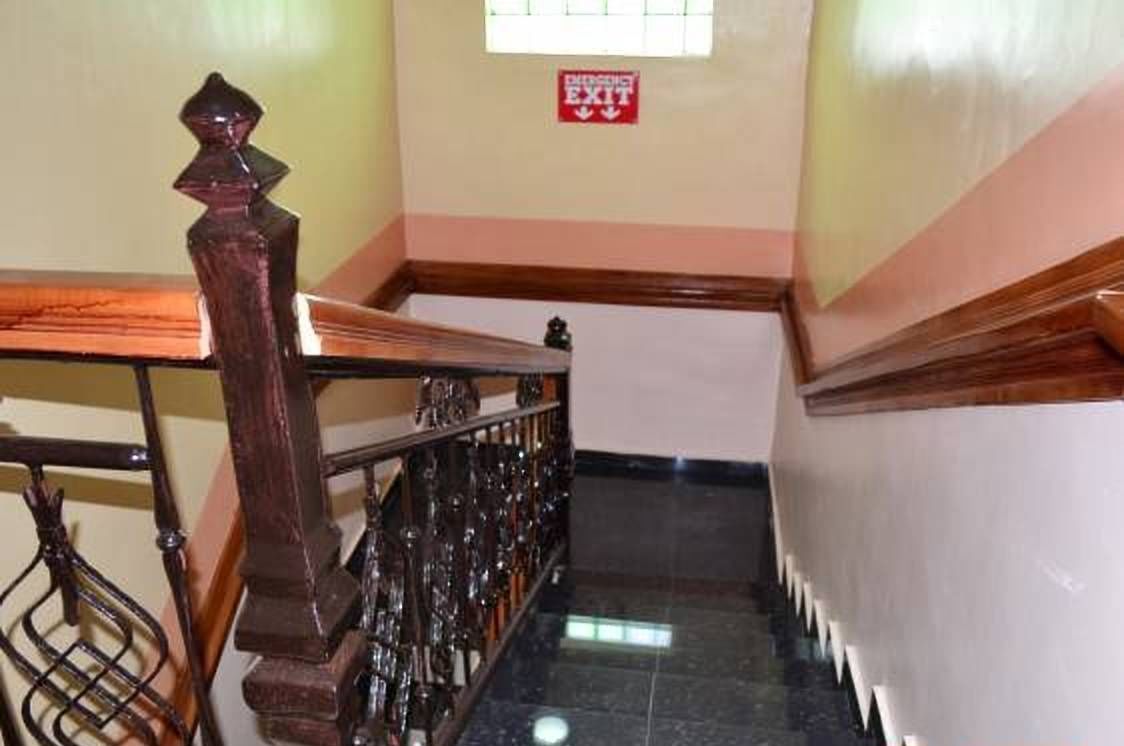 A staircase with a wooden handrail and a red emergency exit sign on the wall.