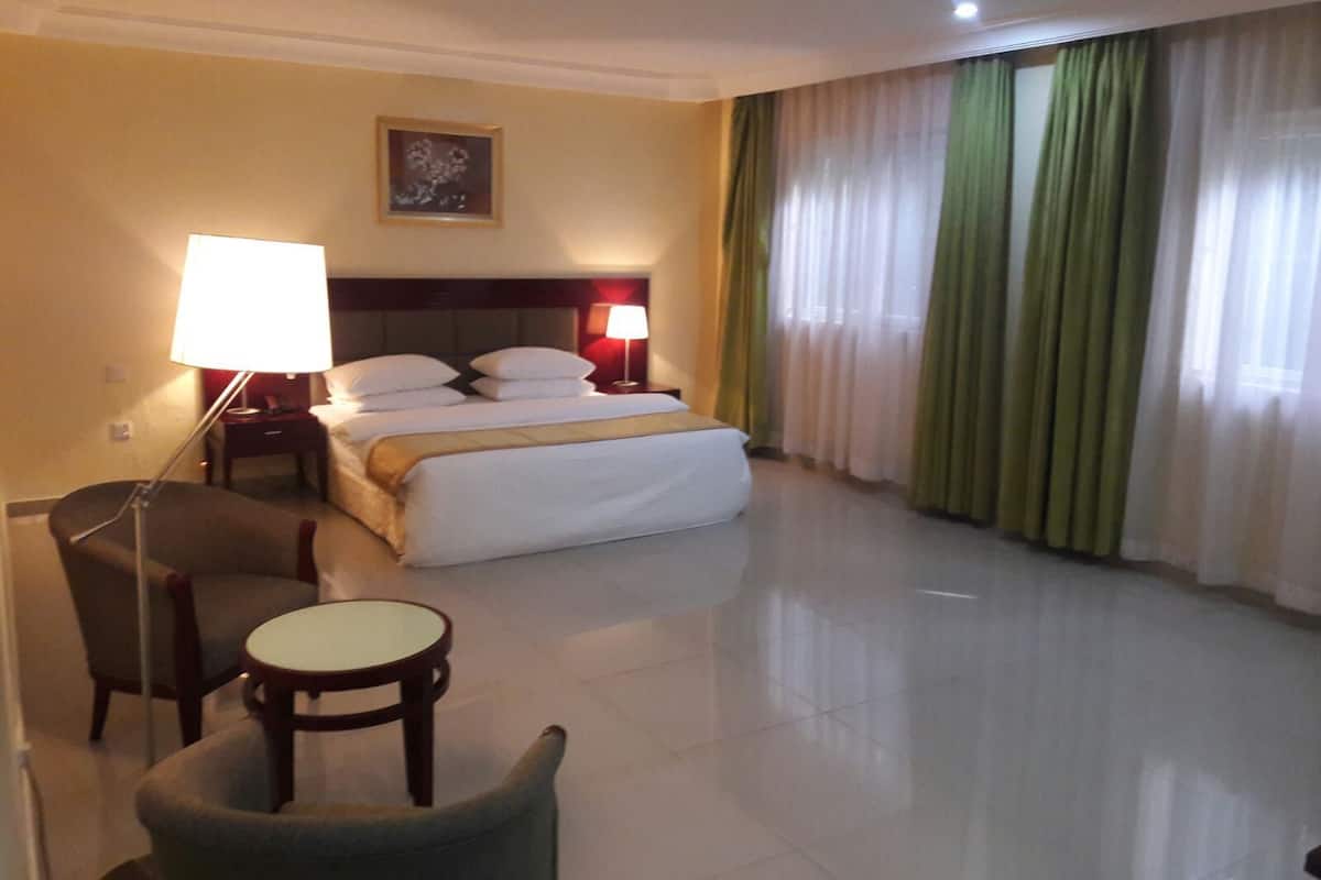 Habitación de hotel con cama, dos lámparas de noche, una silla, una mesita y un cuadro en la pared.