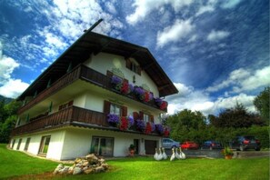 Ein zweistöckiges Gebäude mit Balkonen, einem geneigten Dach und einem Garten mit einer Steinmauer und weißen Schwänen.