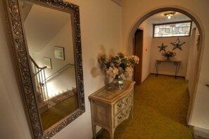 Un passadís amb un mirall, un taulell amb un ram de flors i una escala.