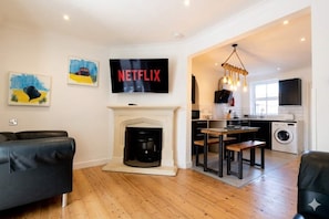 Un salon avec une cheminée, un coin repas, une cuisine et un téléviseur affichant le logo « NETFLIX ».