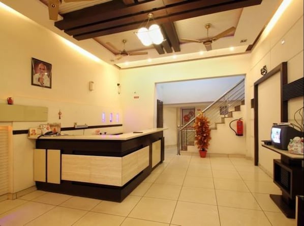 A modern hotel lobby with a reception desk, a staircase, and a fire extinguisher.