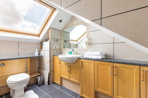 A modern bathroom with a skylight, a freestanding sink, and wooden cabinets.
