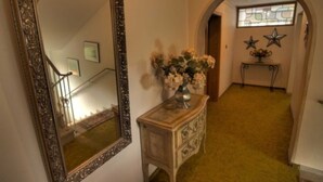 Een gang met een spiegel, een dressoir met een bloevas en een trap.