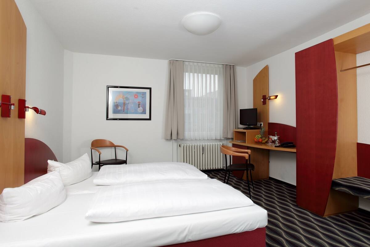 A hotel room with a bed, a desk, a chair, a TV, and a framed picture on the wall.