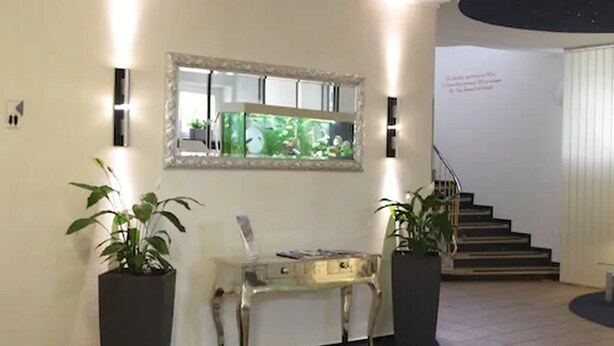 Un vestíbulo moderno con una mesa consola de vidrio, dos plantas en macetas, un espejo grande y una escalera.
