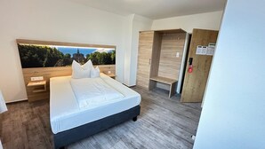 Un dormitorio moderno con cama, mesitas de noche, un armario y un amplio ventanal con vista a un edificio.