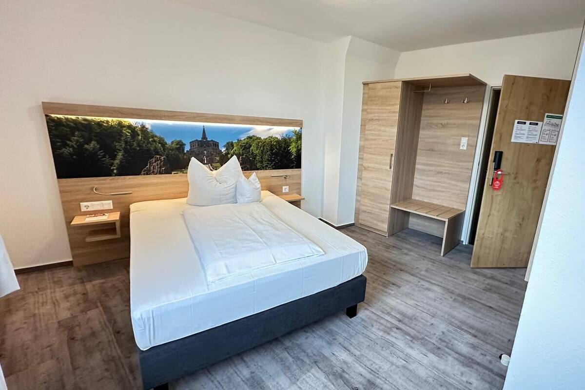 A modern bedroom with a bed, bedside tables, a wardrobe, and a large window with a view of a building.