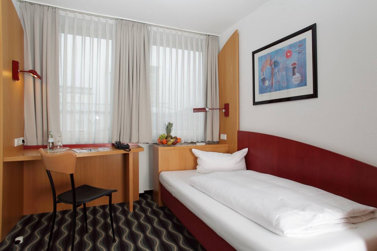A hotel room with a bed, desk, chair, and a window with curtains.