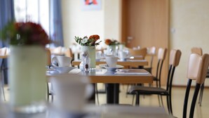 Comedor con mesas dispuestas para el servicio, vajilla blanca y un florero con flores.