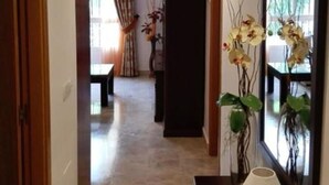 A hallway with a wooden door on the left, a dark console table with a lamp and a mirror on the right, and a view into a dining area with a table and chairs. - Apartment in La Carihuela, Wifi & 20 meters from the beach (Torremolinos)