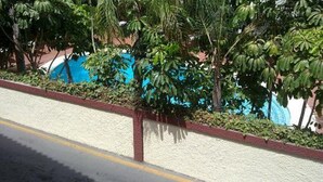 A pool surrounded by lush greenery and a white wall with a red trim. - Apartment in La Carihuela, Wifi & 20 meters from the beach (Torremolinos)