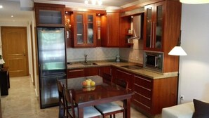 A compact kitchen with wooden cabinets, a stainless steel refrigerator, a microwave, and a dining table with chairs. - Apartment in La Carihuela, Wifi & 20 meters from the beach (Torremolinos)