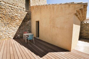 Una terraza de madera con una mesa y sillas, un muro de piedra y un edificio color beige.